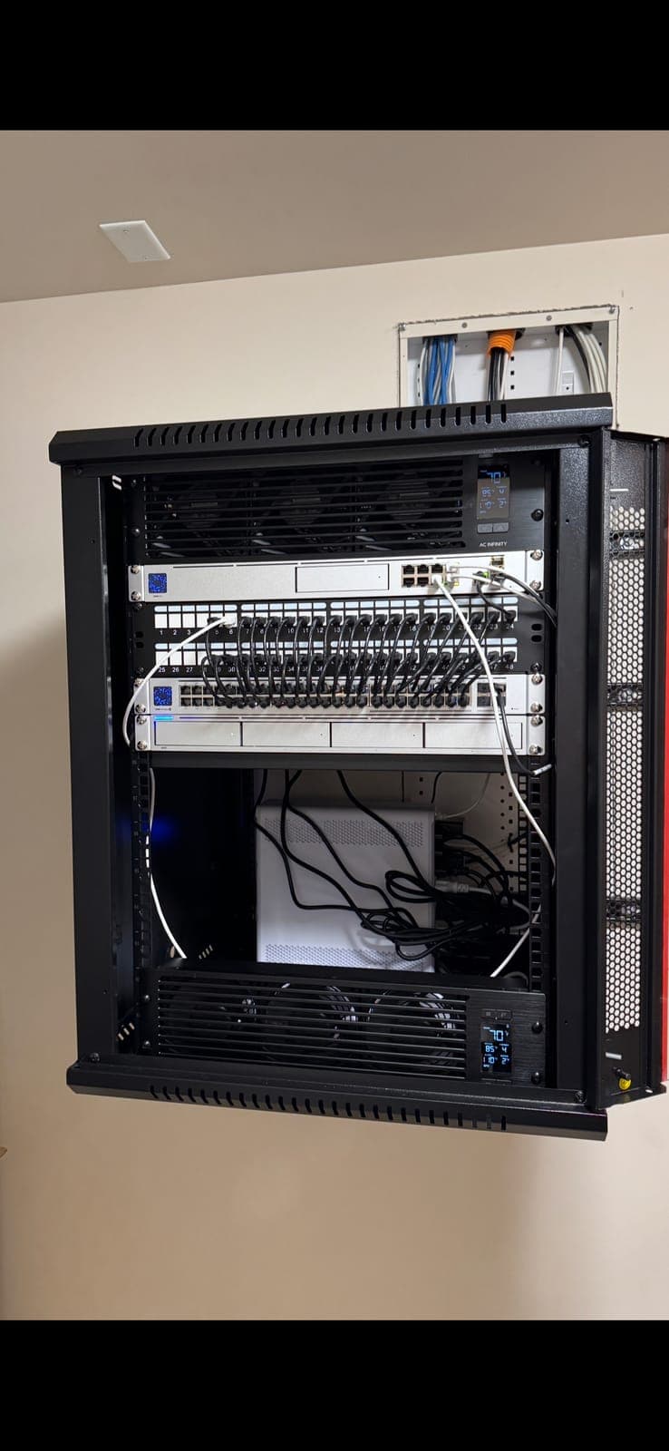 Wall-mounted network rack with UniFi gateway, patch panel, and cooling